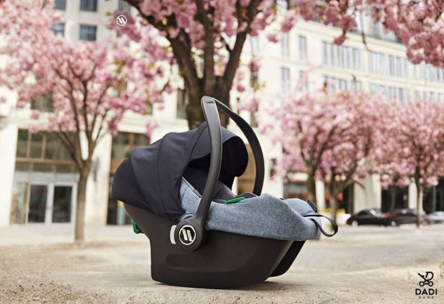 Pierwszy fotelik samochodowy dla noworodka 0-13 kg na tle kwitnących drzew, gotowy do podróży.